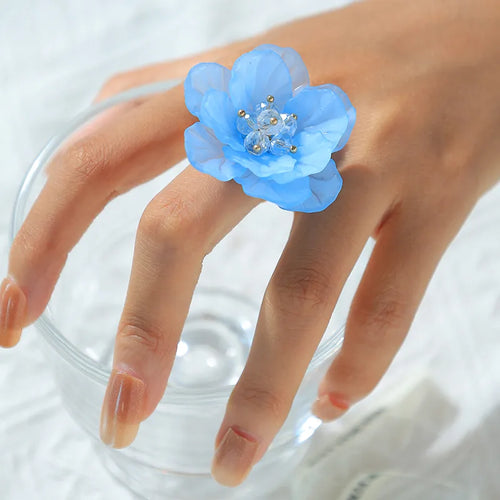 Hand wearing a blue floral ring on a white background