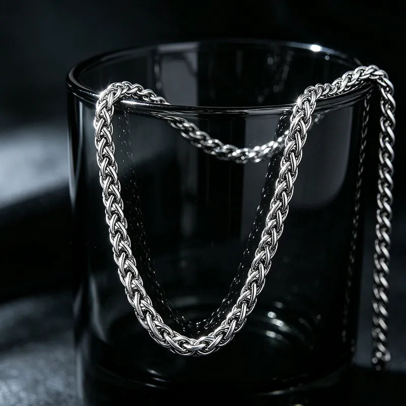 A silver-toned multi-strand chain necklace draped over a dark, translucent glass tumbler against a black background.