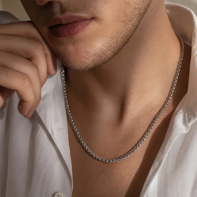A close-up of a man wearing a silver-toned chain necklace with a white button-down shirt.