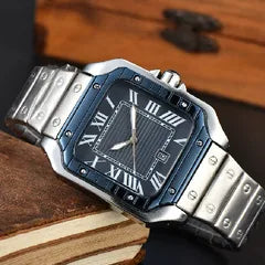 A stainless steel analog watch with a blue dial and silver-tone metal bracelet, resting on a wooden surface next to an open book.