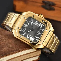 A gold-tone stainless steel watch with a black dial, Roman numeral hour markers, and a matching gold-tone link bracelet, resting on a brown leather book cover.