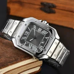 A silver-tone metal watch with a square bezel, black dial, and Roman numeral hour markers, resting on a dark wooden surface.