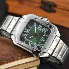 A stainless steel analog watch with a green dial and Roman numeral hour markers, resting on a vintage book with a wooden background.