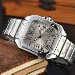 A stainless steel analog watch with a silver-tone band and a silver dial featuring black Roman numerals, resting on a vintage brown leather-bound book.