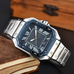 A men's stainless steel watch with a dark blue bezel and dial, Roman numeral hour markers, and a silver link bracelet, resting on a vintage book with a wooden box in the background.