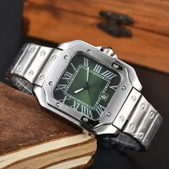 A silver-toned metal watch with a green dial and Roman numeral hour markers, resting on a stack of vintage books against a dark wooden background.