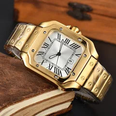 A gold-tone stainless steel watch with a square silver dial, Roman numeral hour markers, and a matching gold-tone metal link bracelet, resting on a vintage brown leather book.