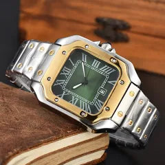 A men's analog watch with a silver stainless steel link bracelet, a gold-tone bezel, and a dark green dial with Roman numerals, resting on a vintage book.