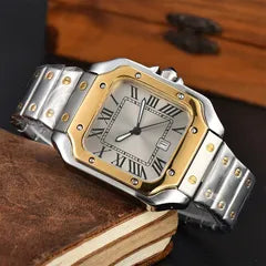 A men's stainless steel and gold-tone watch with a silver dial and Roman numeral hour markers, resting on a vintage brown leather-bound book.