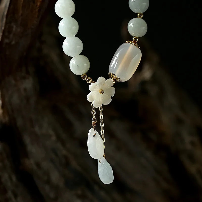 Pale beaded bracelet displayed with floral detail and hanging teardrop charms