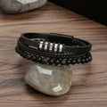 Black layered bracelet with dark beads and silver-tone accents on a stone