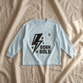 Pale-blue Born Bold T-shirt on linen bedsheets