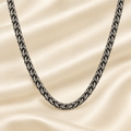 A dark gunmetal gray oxidized chain necklace draped in a U-shape over a cream-colored satin fabric background.