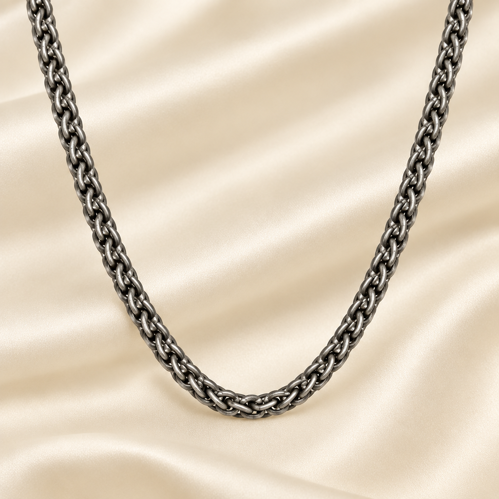 A dark gunmetal gray oxidized chain necklace draped in a U-shape over a cream-colored satin fabric background.