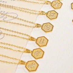 Gold hexagonal pendant necklaces with engraved zodiac symbols, shown on a light cream background.